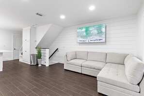 A modern living room with a sofa, a staircase, a potted plant, and a wall-mounted TV. - Emerald Hideout (Miramar Beach)