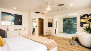Ein modernes Schlafzimmer mit einem großen Bett, einer Sitzecke mit einem Sessel, einer Badewanne und Kunstwerken an den Wänden.