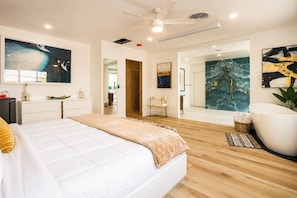 Ein modernes Schlafzimmer mit einem großen Bett, einer Sitzecke mit einem Sessel, einer Badewanne und Kunstwerken an den Wänden.