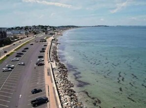 Una carretera costera con un estacionamiento, una playa y una vista despejada del océano.
