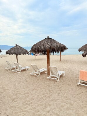 Ein Strand mit Reetdachschirmen und weißen Liegestühlen.