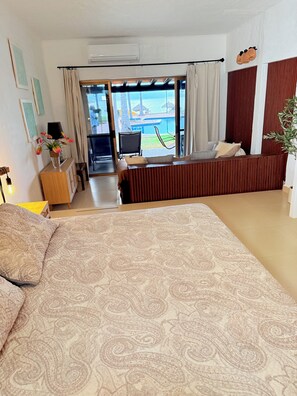 Ein Hotelzimmer mit Bett, Schreibtisch, Stuhl und Blick auf den Pool, sowie einer Klimaanlage.