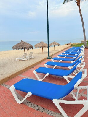 Eine Strandlounge mit Liegestühlen, Strohsonnenschirmen und Blick auf das Meer.