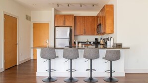 Una cocina moderna con armarios de madera, un refrigerador de acero inoxidable, un microondas y una barra con cuatro taburetes.