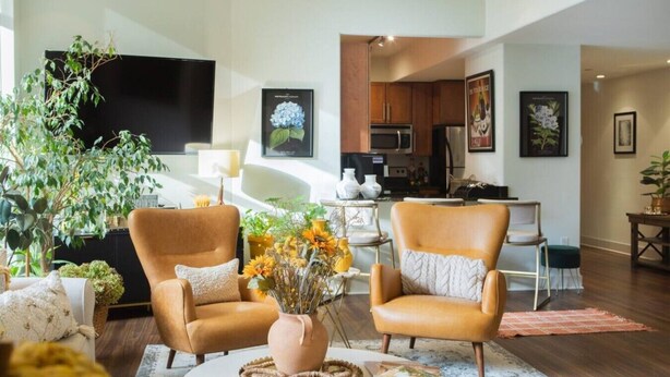 Una sala de estar con dos sillones de cuero, una mesita de centro y un comedor, con una cocina al fondo.