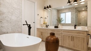 Un baño moderno con una bañera independiente, armarios de madera, un espejo grande y un florero en el tocador.