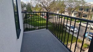 Un balcón con vista a una calle residencial, un jardín y coches aparcados.