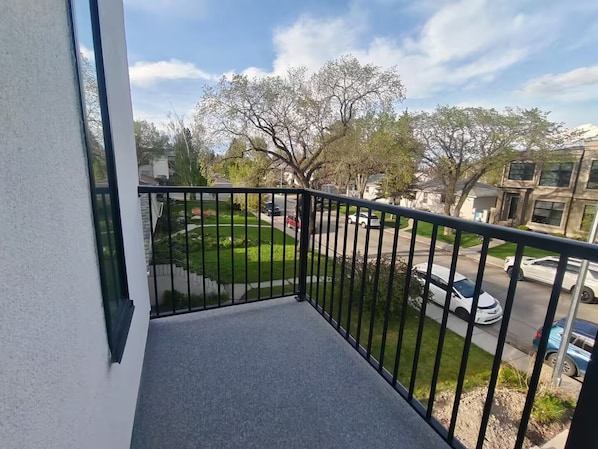A balcony with a view of a residential street, a lawn, and parked cars.