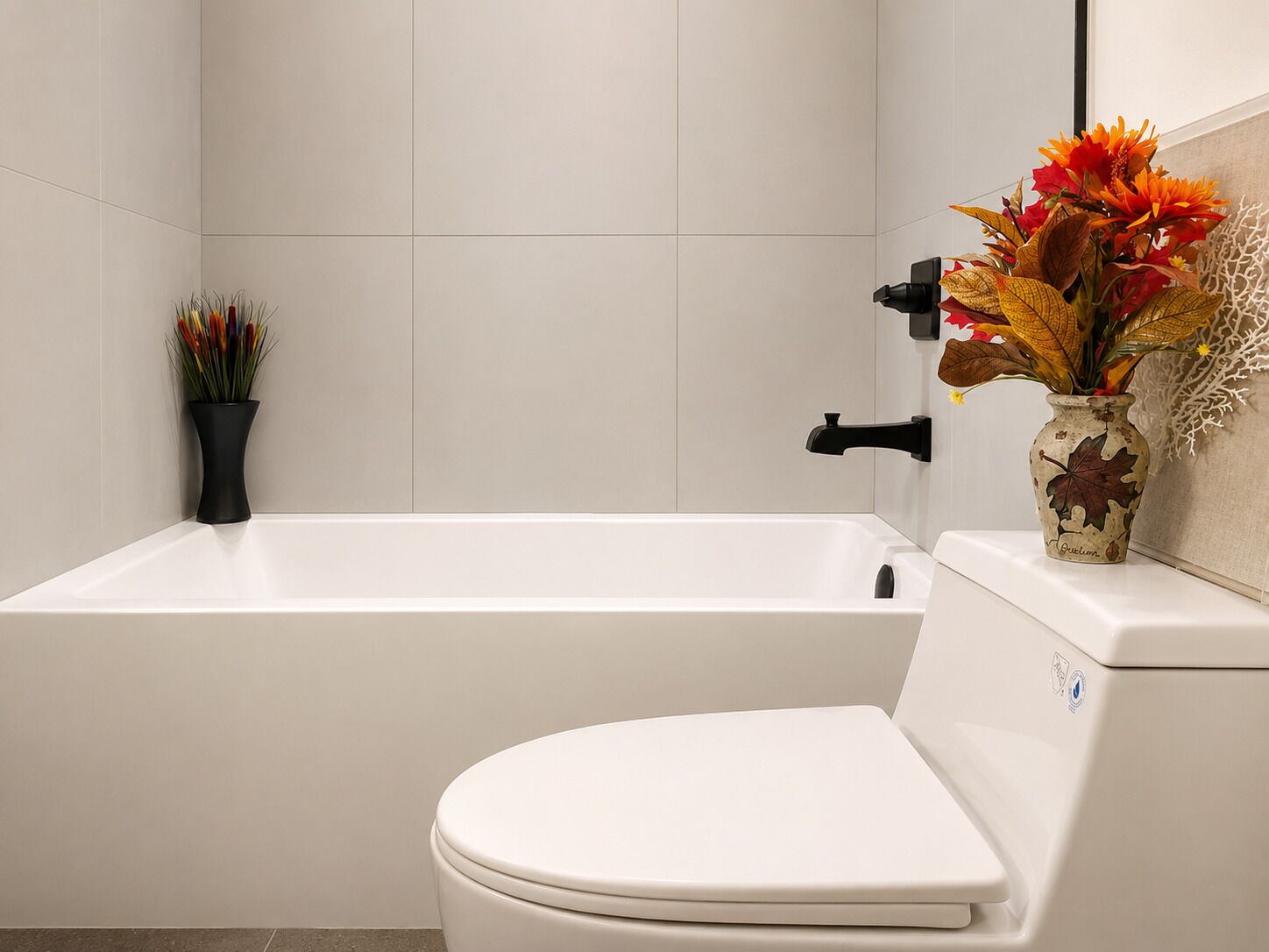 A bathroom with a white bathtub, a toilet, and a vase with flowers on the wall.