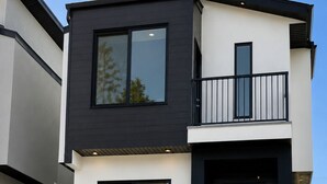 Una casa moderna de dos pisos con balcón, ventanas grandes y puerta principal.