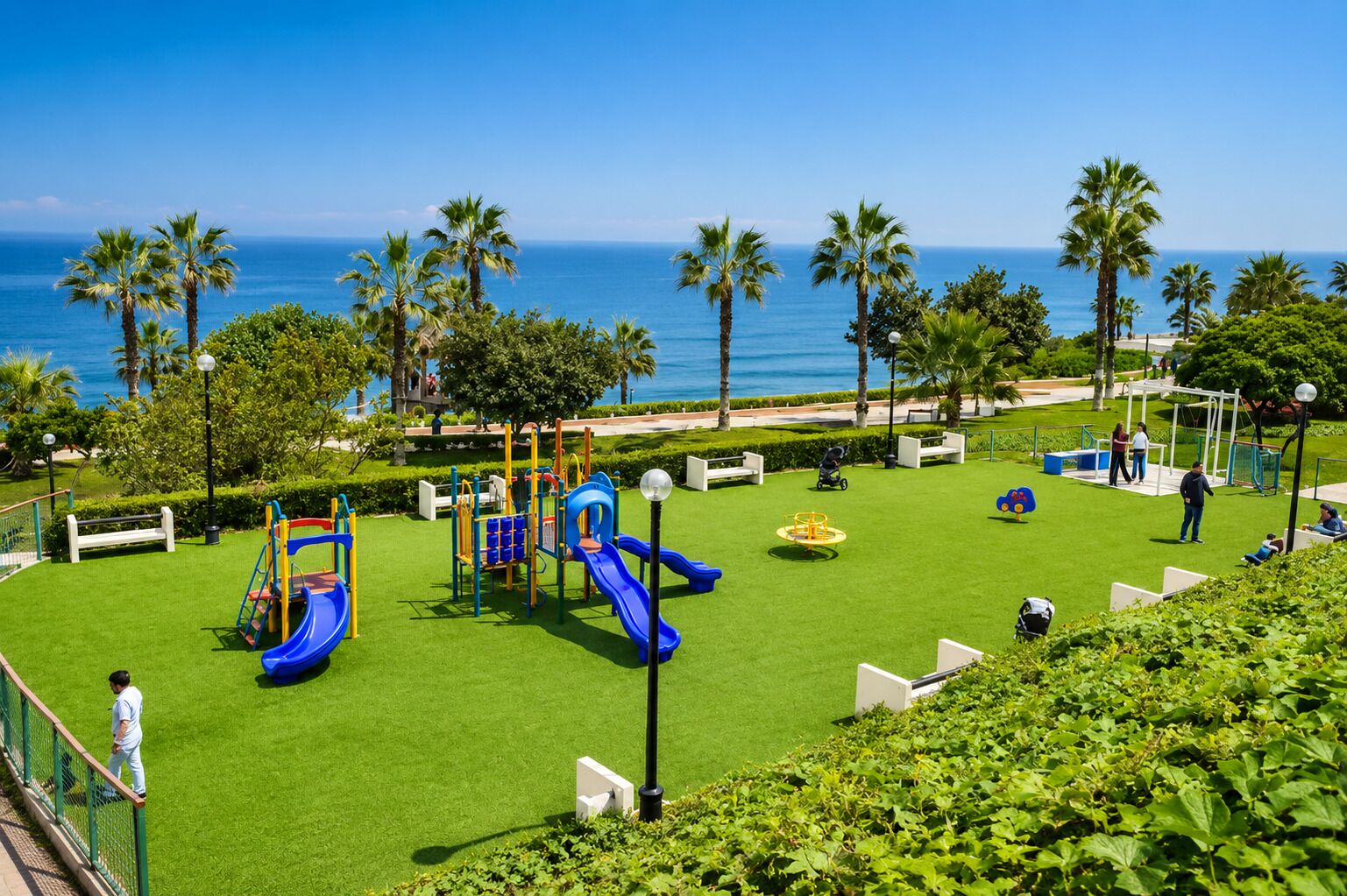 A playground with slides and climbing structures, surrounded by palm trees and a view of the ocean.