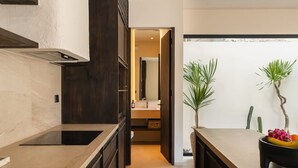 Eine moderne Küche mit dunklen Schränken, einer Marmorarbeitsplatte und Blick ins angrenzende Badezimmer.