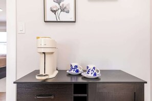 Eine Kaffeemaschine, zwei Tassen und ein gerahmtes Kunstwerk auf einem dunklen Holztisch.