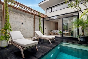 Ein moderner Poolbereich im Freien mit zwei Liegestühlen, einer Steinwand und einer Holzpergola.