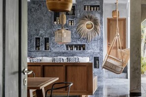 Een modern interieur met een houten eettafel, een bank met gestreepte kussens en een hangende rieten stoel.