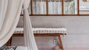 A bedroom with a bed, a bench, a hanging light fixture, a wooden partition, and a window with a view of a fence and plants. - Architectural 2 bedroom Pool Villa Berawa (Kecamatan Kuta Utara)