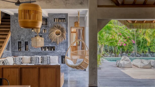 A modern interior with a wooden dining table, a hanging chair, and a view of an outdoor garden with a pool. - Architectural 2 bedroom Pool Villa Berawa (Kecamatan Kuta Utara)
