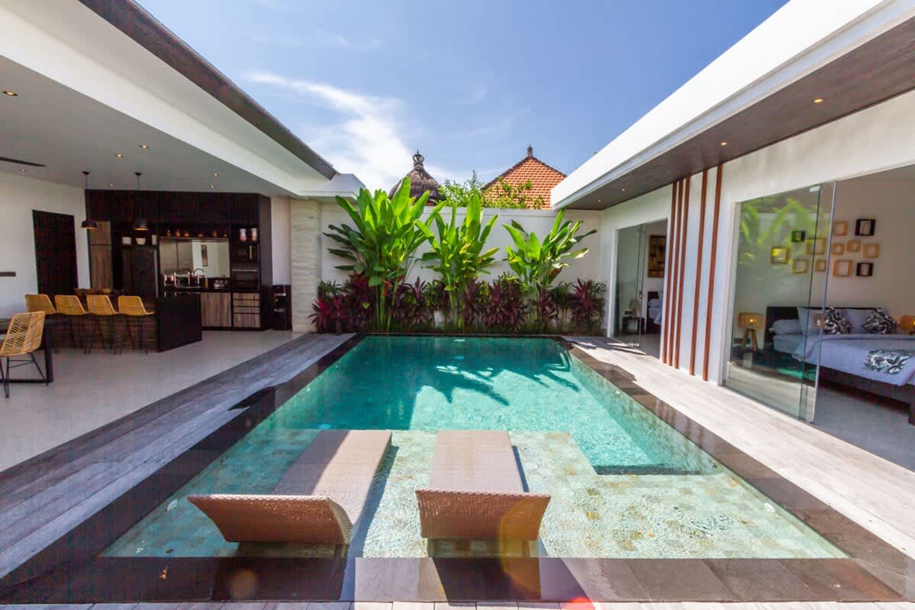 A modern pool area with lounge chairs, a bar, and a dining area.