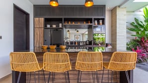 A modern kitchen with a central island, built-in appliances, and a dining area with wicker chairs. - Cozy 3BR Villa w  Private Pool near Berawa Beach (Kecamatan Kuta Utara)