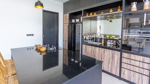 A modern kitchen with a central island, black countertops, wooden cabinetry, and pendant lighting. - Cozy 3BR Villa w  Private Pool near Berawa Beach (Kecamatan Kuta Utara)