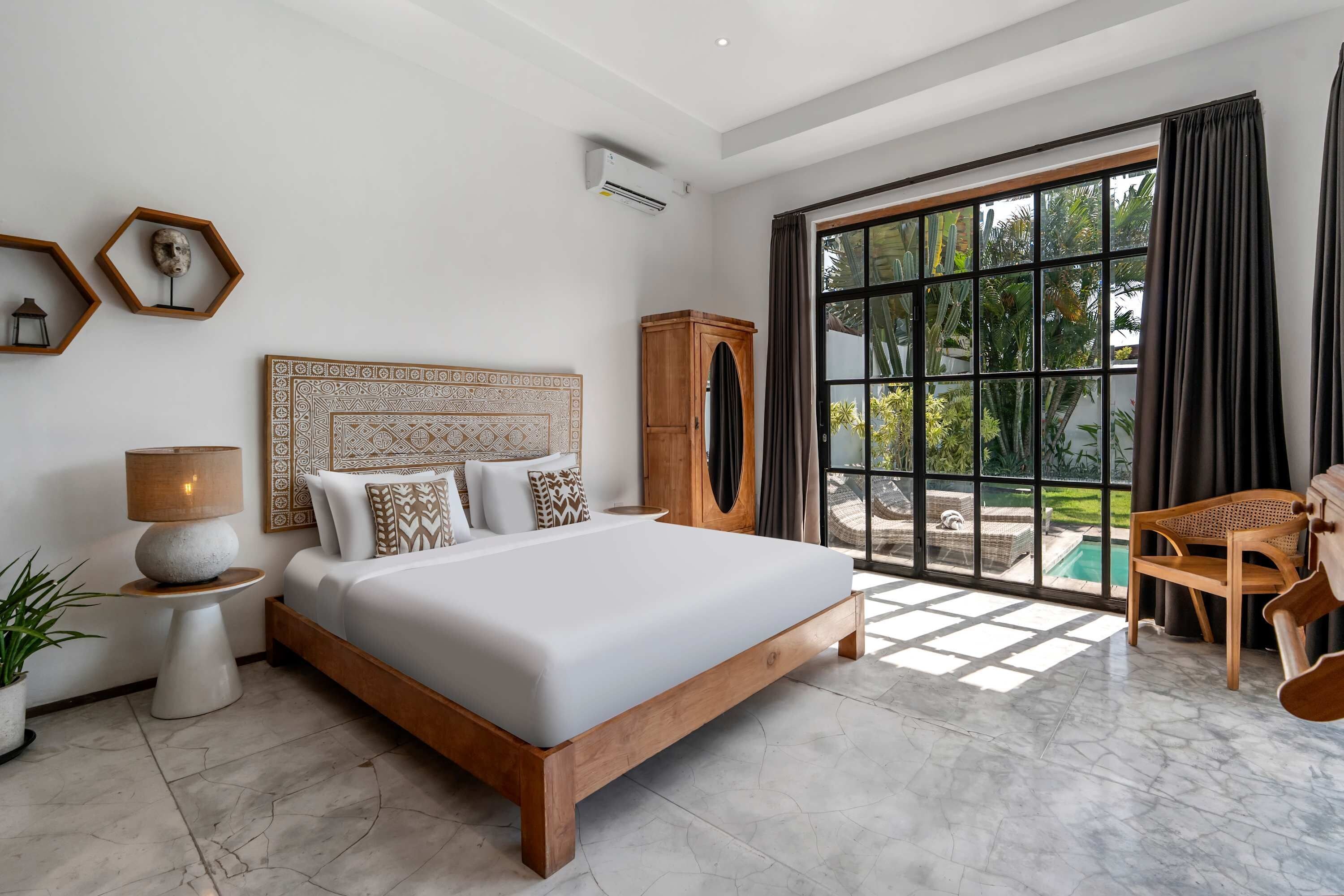 Un dormitorio moderno con una cama grande, una mesita de noche, una lámpara, un armario de madera y vistas a una piscina a través de un ventanal amplio.