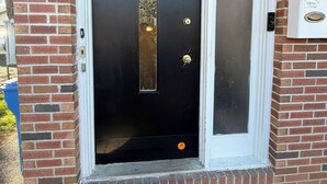 Une porte noire avec une petite fenêtre, une boîte aux lettres et un paillasson.