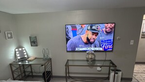 Une chambre à coucher avec un lit, une coiffeuse avec éclairage, un téléviseur fixé au mur et une petite table sur laquelle est posé un objet décoratif.