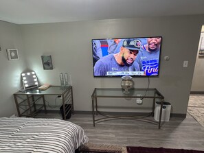 Ett sovrum med en säng, en sminkbord med belysning, en tv på väggen och ett litet bord med en dekorativ prydnad.