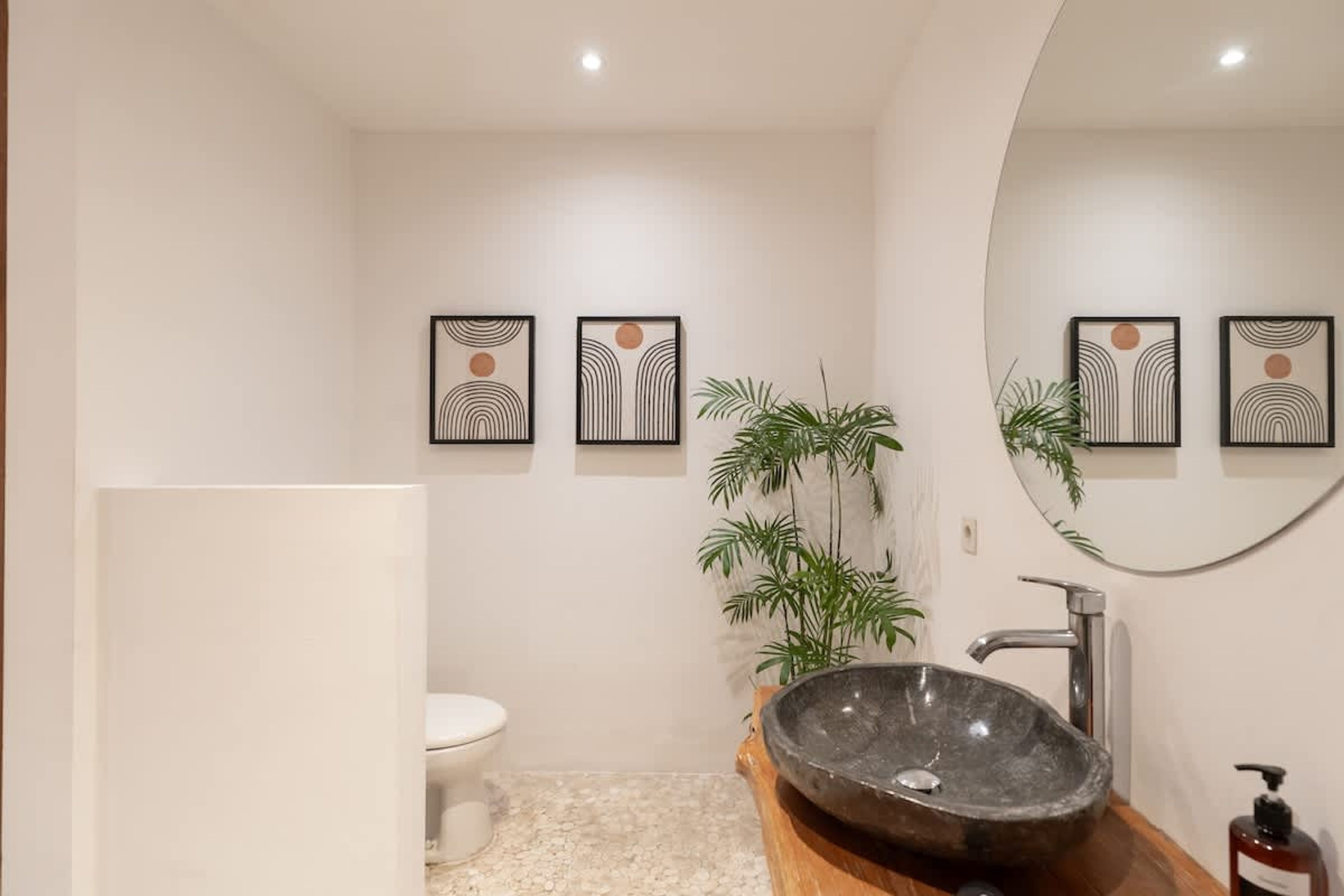 A modern bathroom with a stone sink, toilet, and framed artwork on the wall.