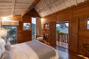 Ein Zimmer mit Holzboden, einem Bett, einem Sessel und einem Balkon mit Geländer.