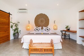 Ein Schlafzimmer mit Bett, Nachttischen, Schreibtisch, Stuhl, einer Pendelleuchte und einer Wand-Klimaanlage.