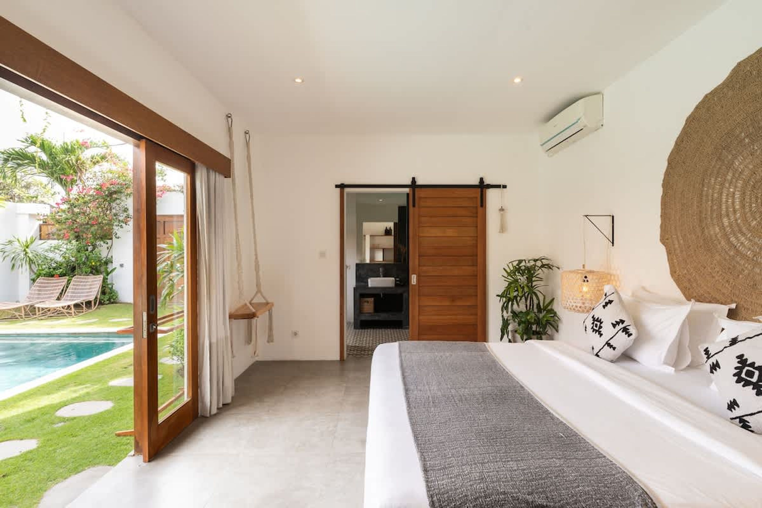 A bedroom with a large bed, a view of a swimming pool, and a sliding door leading to a bathroom.