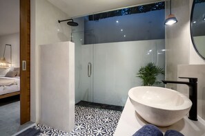 Um banheiro moderno com chuveiro em cabine de vidro, pia branca e ladrilhos estampados.