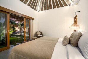 Een slaapkamer met een groot bed, een nachtkastje, een lamp en uitzicht op een tuin door glazen deuren.