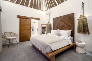 Quarto com cama de madeira, luminária pendente, sanita branca e cadeira de vime.