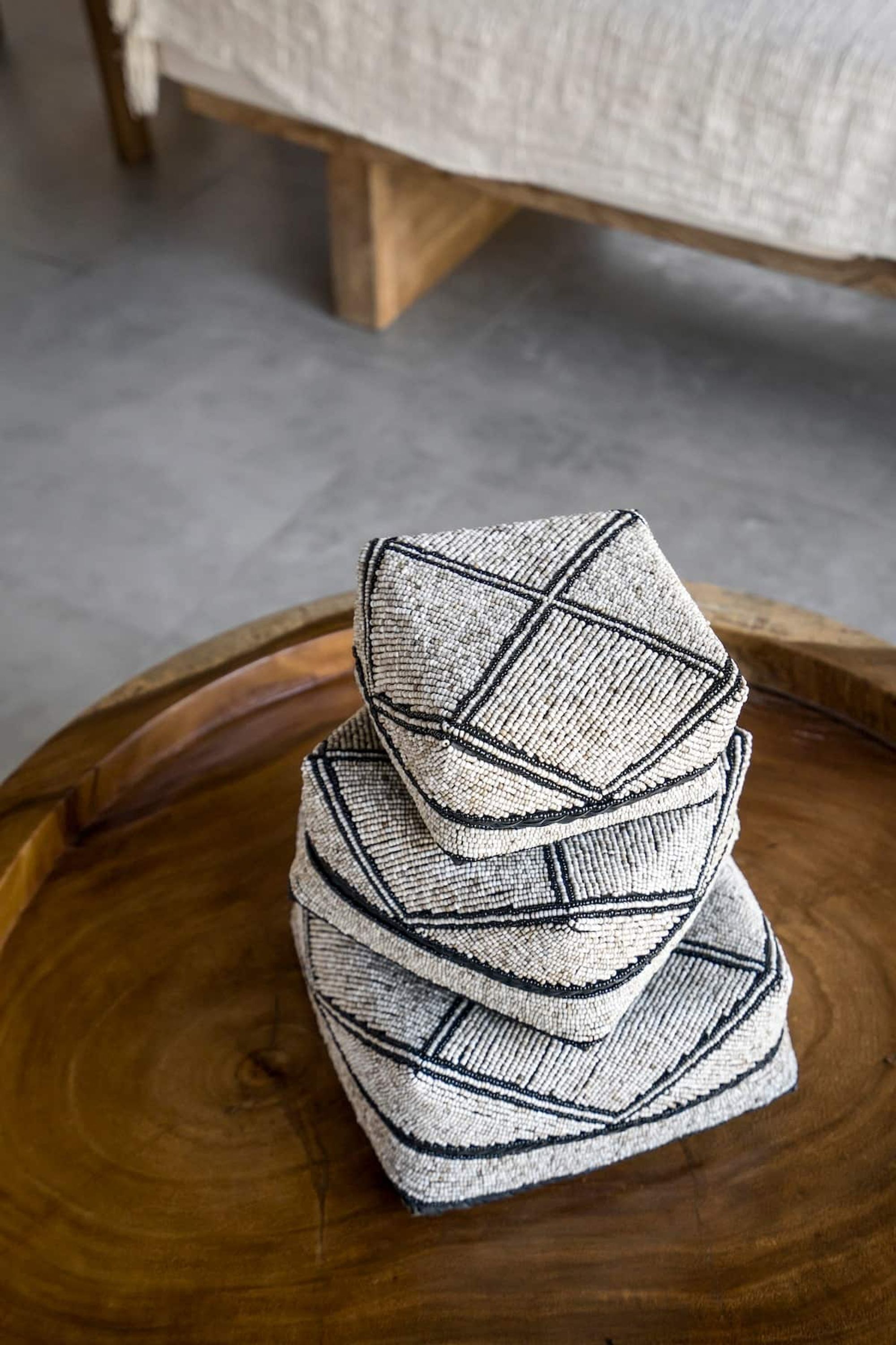 Une pile de coussins aux motifs géométriques posée sur une table ronde en bois.