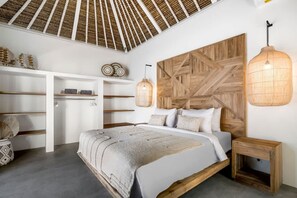 Ein Schlafzimmer mit einem hölzernen Kopfteil, einem Bett mit grauer Decke, einem Nachttisch aus Holz und einer Pendelleuchte.