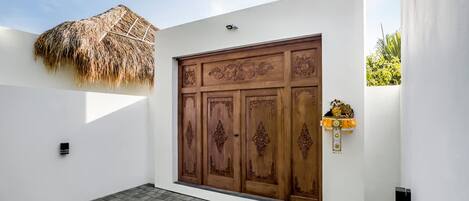 A white building with a large wooden door, a thatched roof, and a paved courtyard.