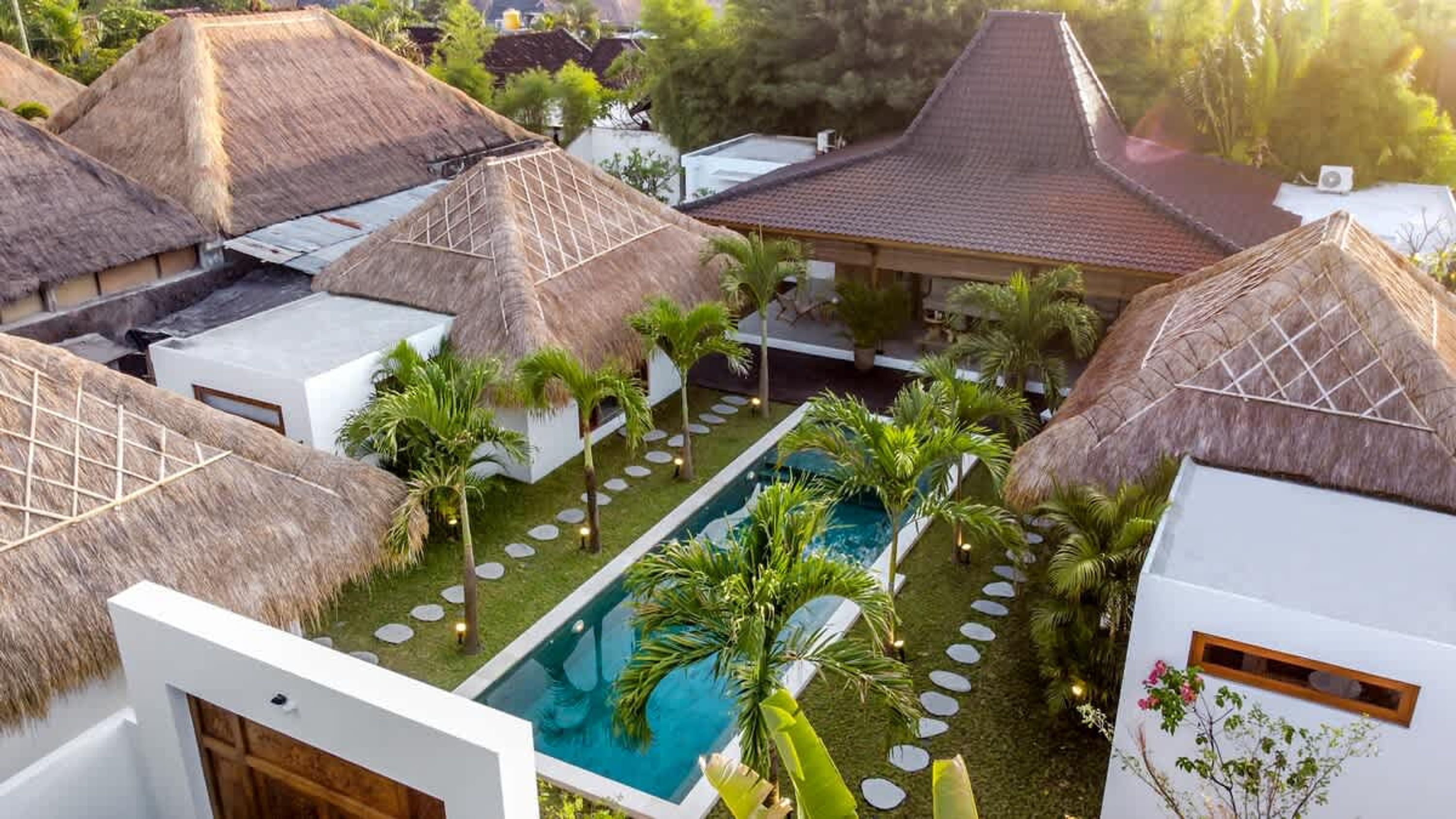 A resort with thatched-roof buildings, a swimming pool, and palm trees.
