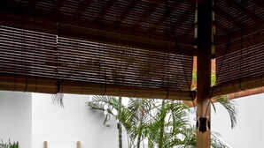 Un patio con mobiliario de mimbre, una mesa de madera y una escalera blanca que lleva a un nivel superior.