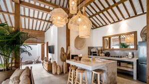 Una cocina amplia con una isla grande, vigas de techo de madera e iluminación colgante de mimbre.