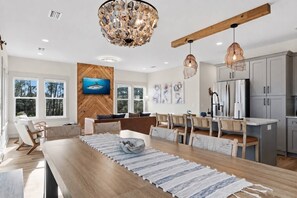 Una cocina moderna con vigas de madera, un comedor con una mesa larga y un ventanal con vistas a árboles.