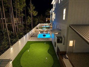 A well-lit backyard with a swimming pool, a grassy area, and a wooden deck. - Pool, Putting Green, Giant Sand Pit, Walk 2 Beach (Port St. Joe)