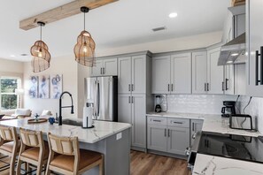 A modern kitchen with grey cabinets, a stainless steel refrigerator, a marble countertop, and two wicker pendant lights. - Pool, Putting Green, Giant Sand Pit, Walk 2 Beach (Port St. Joe)