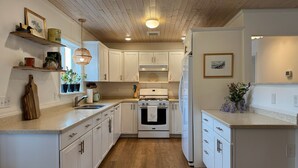 A modern kitchen with white cabinetry, a wooden floor, and a central island. - Coastal Cottage Escape with Sunset Views, Near Beach, Bay & Wildlife Refuge (Chincoteague)