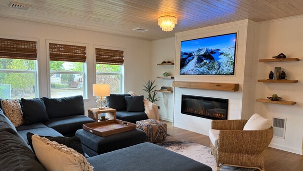 A living room with a sectional sofa, a fireplace, a television, and wooden shelves. - Coastal Cottage Escape with Sunset Views, Near Beach, Bay & Wildlife Refuge (Chincoteague)