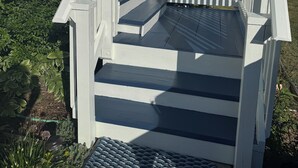 A house with a white exterior, a front porch with a railing, and a staircase leading to the entrance. - Coastal Cottage Escape with Sunset Views, Near Beach, Bay & Wildlife Refuge (Chincoteague)