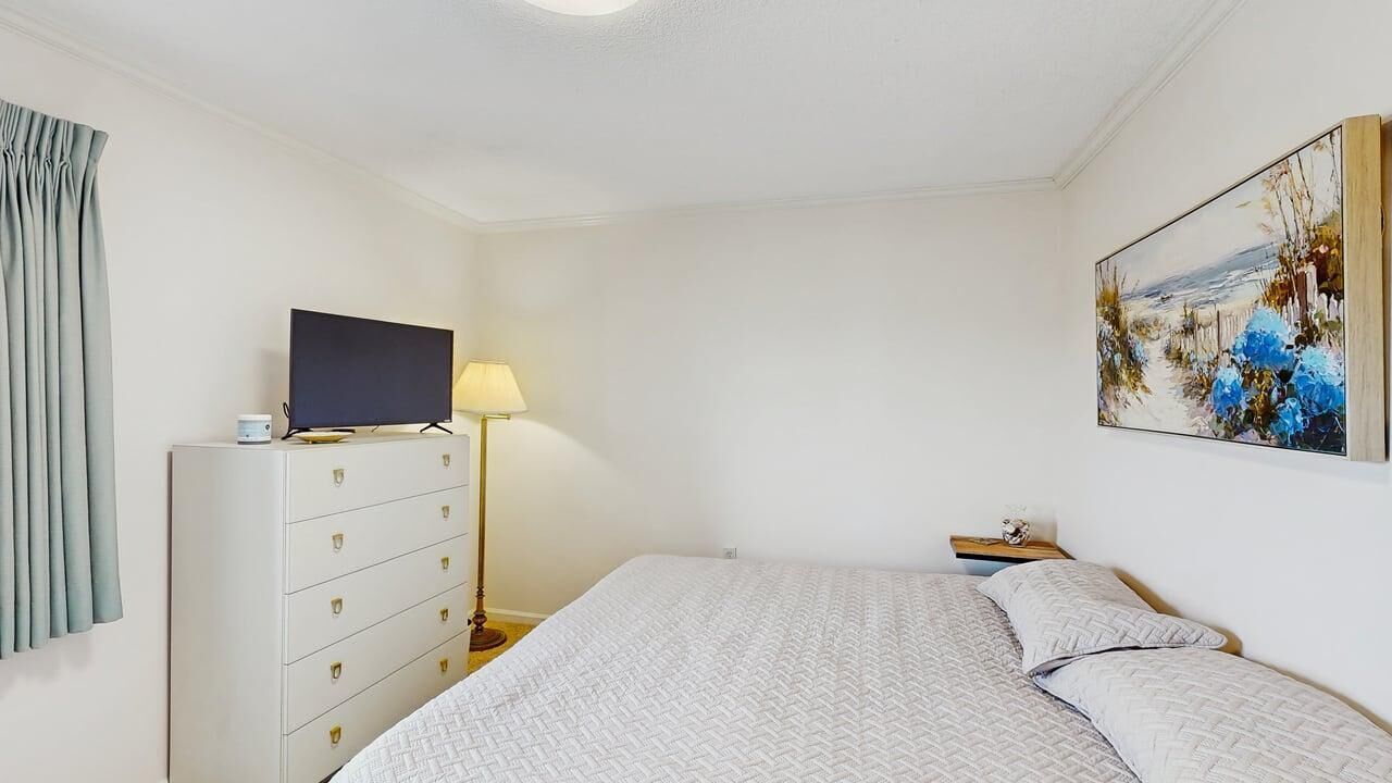 Un dormitorio con una cama, un televisor sobre una cómoda, una lámpara y un cuadro en la pared.