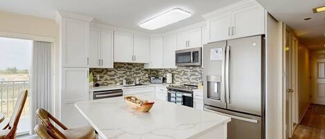 A modern kitchen with white cabinets, a marble island, stainless steel appliances, and a view to the outside.