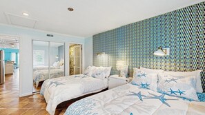 A bedroom with two beds, a mirror, a nightstand, and a patterned wall. - White Marlin 405B (Ocean City)